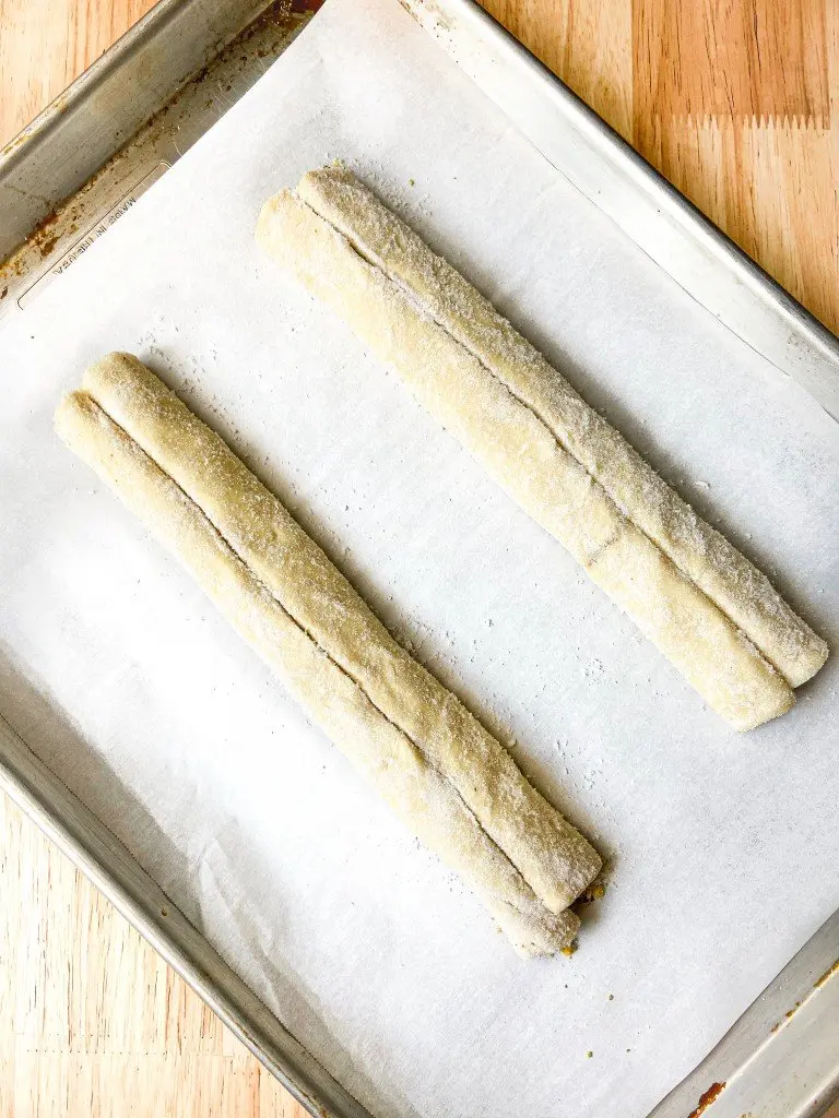 Rolled up puff pastry coated in sugar on a parchment-line sheet tray.