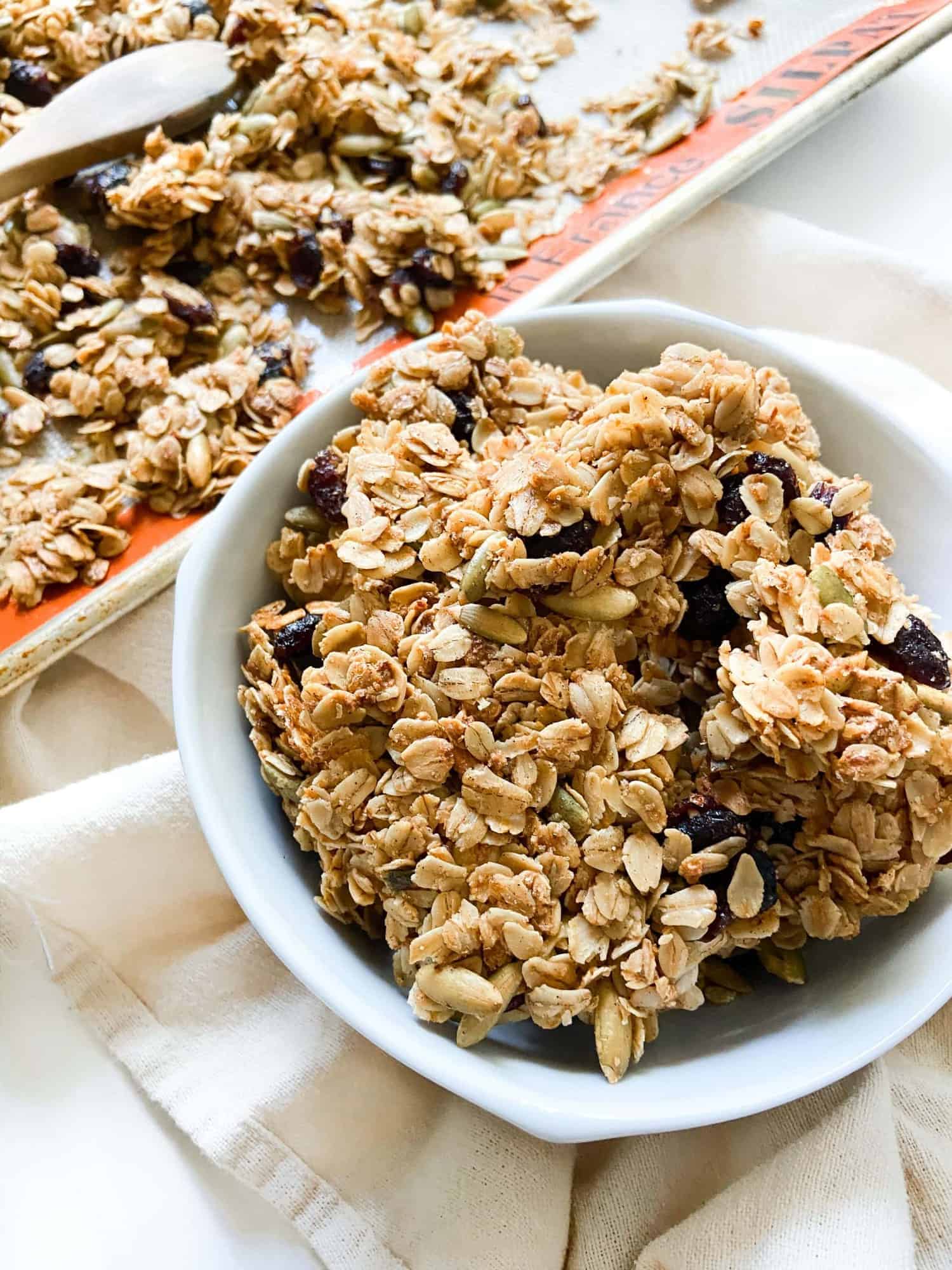 A bowl of pumpkin spice granola next to a sheet tray full of it.
