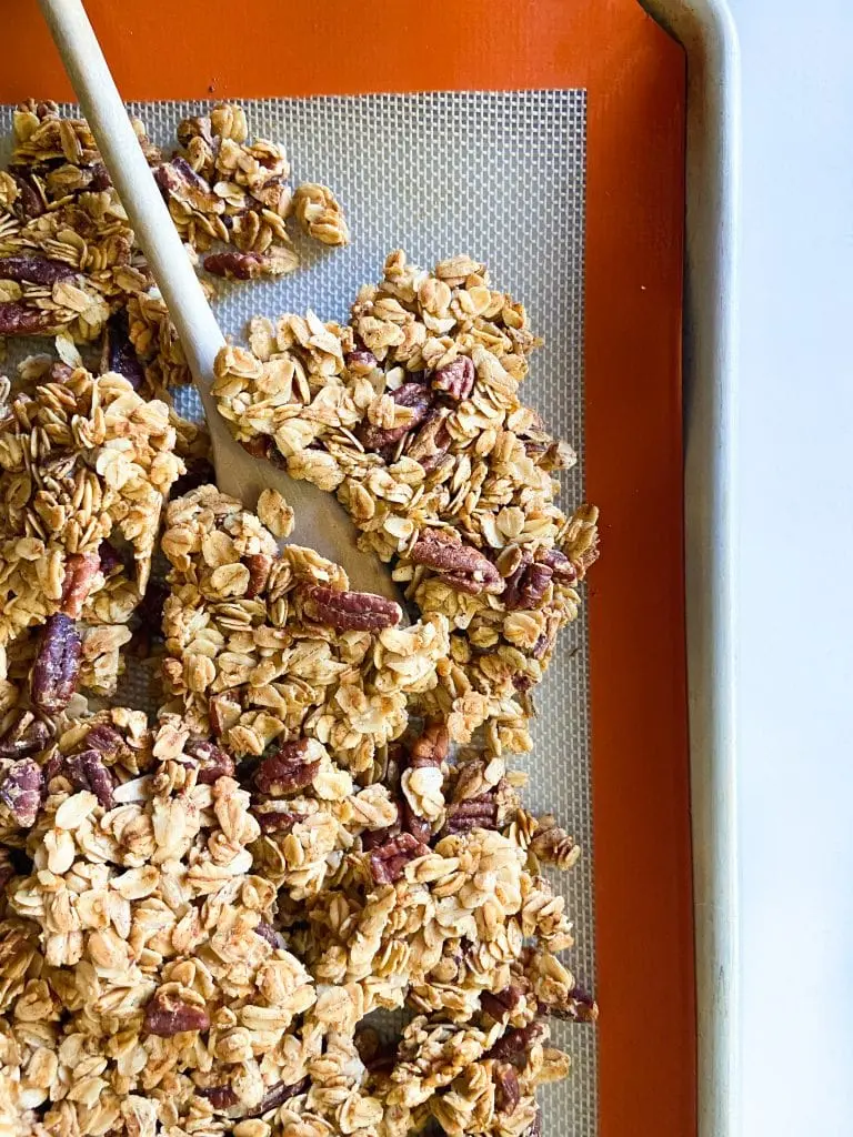 Granola clusters on a Silpat-lined tray with a wooden spoon. 