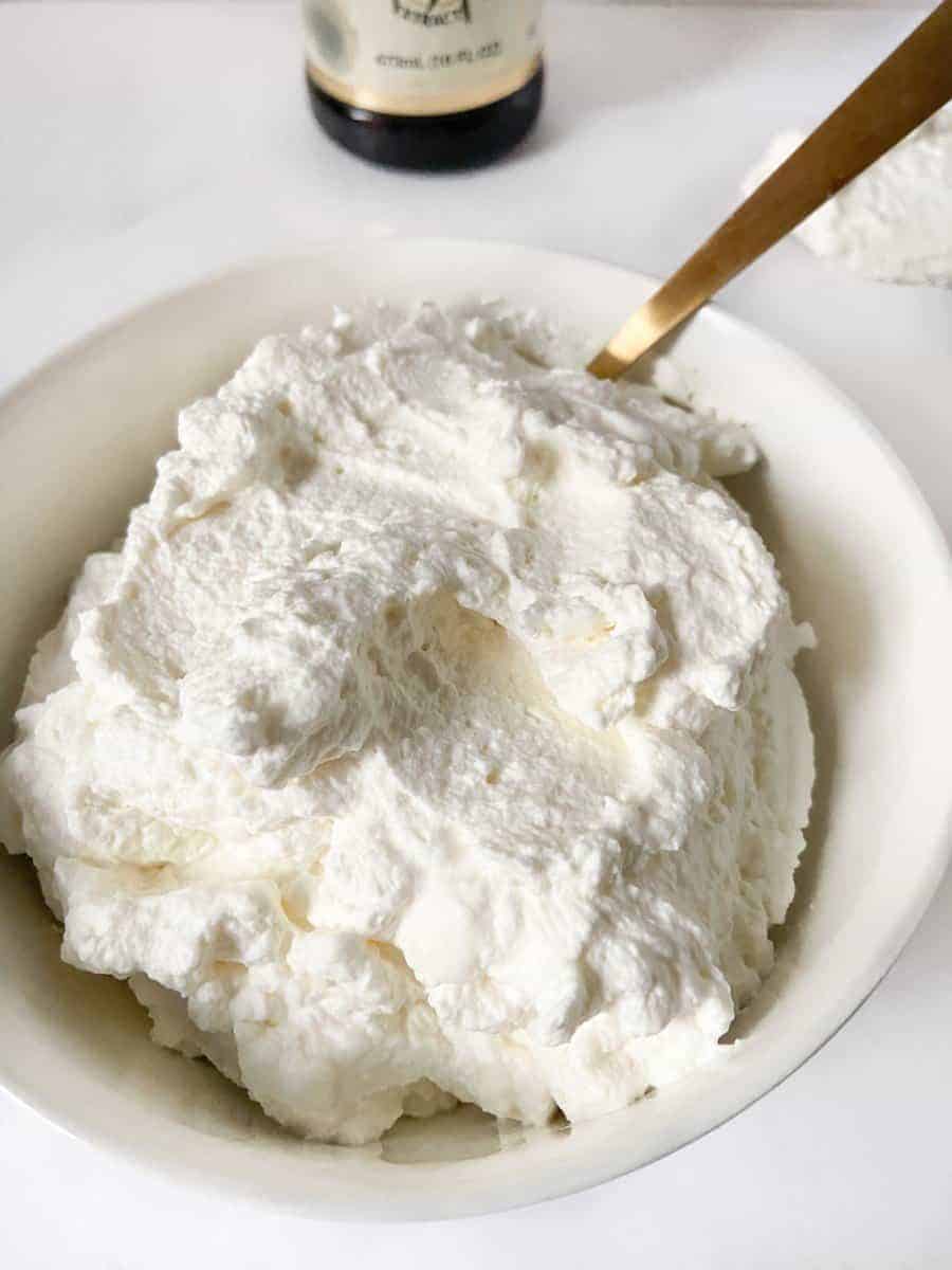 Whipped cream in white bowl with spoon.
