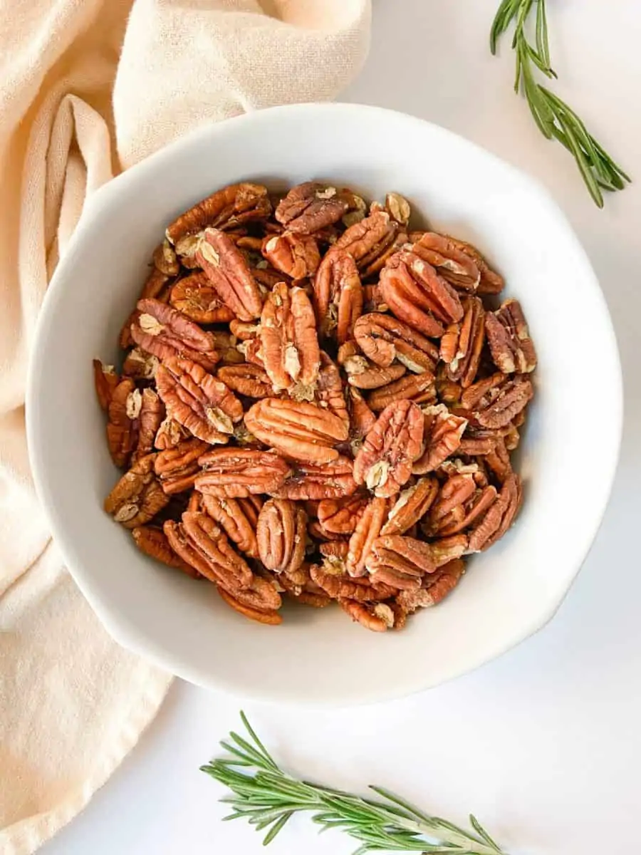 A white bowl of rosemary spiced pecans. 