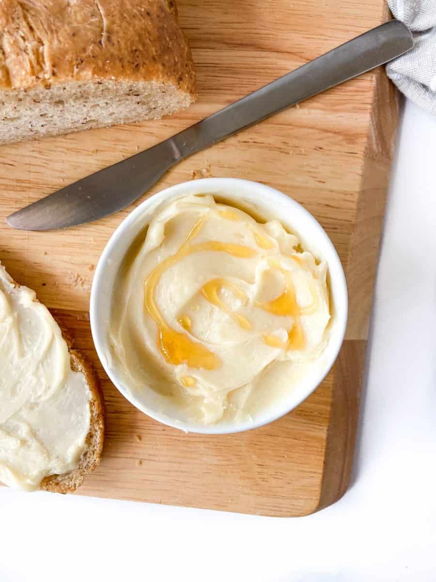 A bowl of butter garnished with honey served with a loaf of bread and a butter knife. 