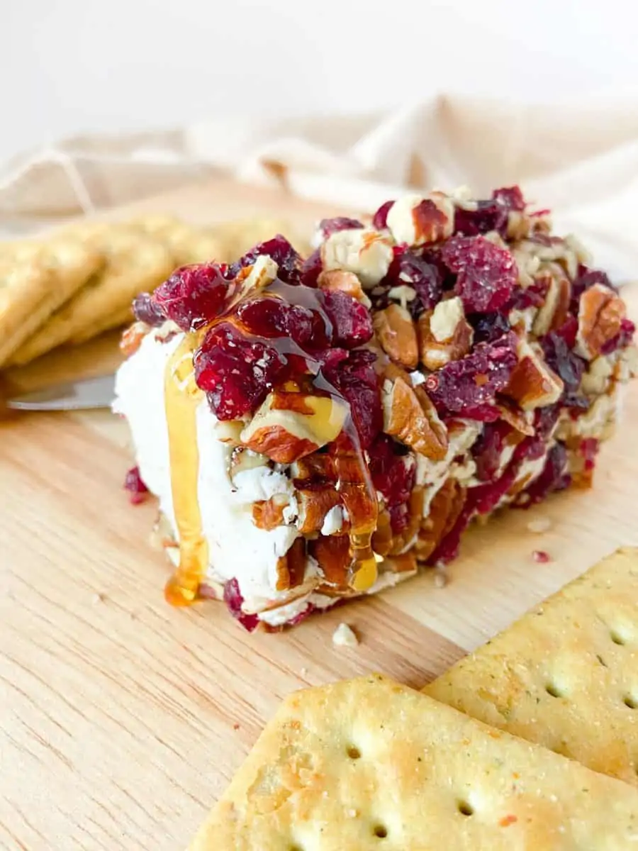 A completed cranberry pecan goat cheese log drizzled with honey and paired with crackers. 