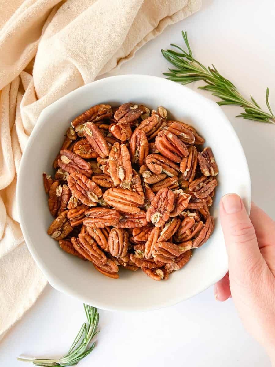 A white bowl of pecans with a hand reaching for them. 