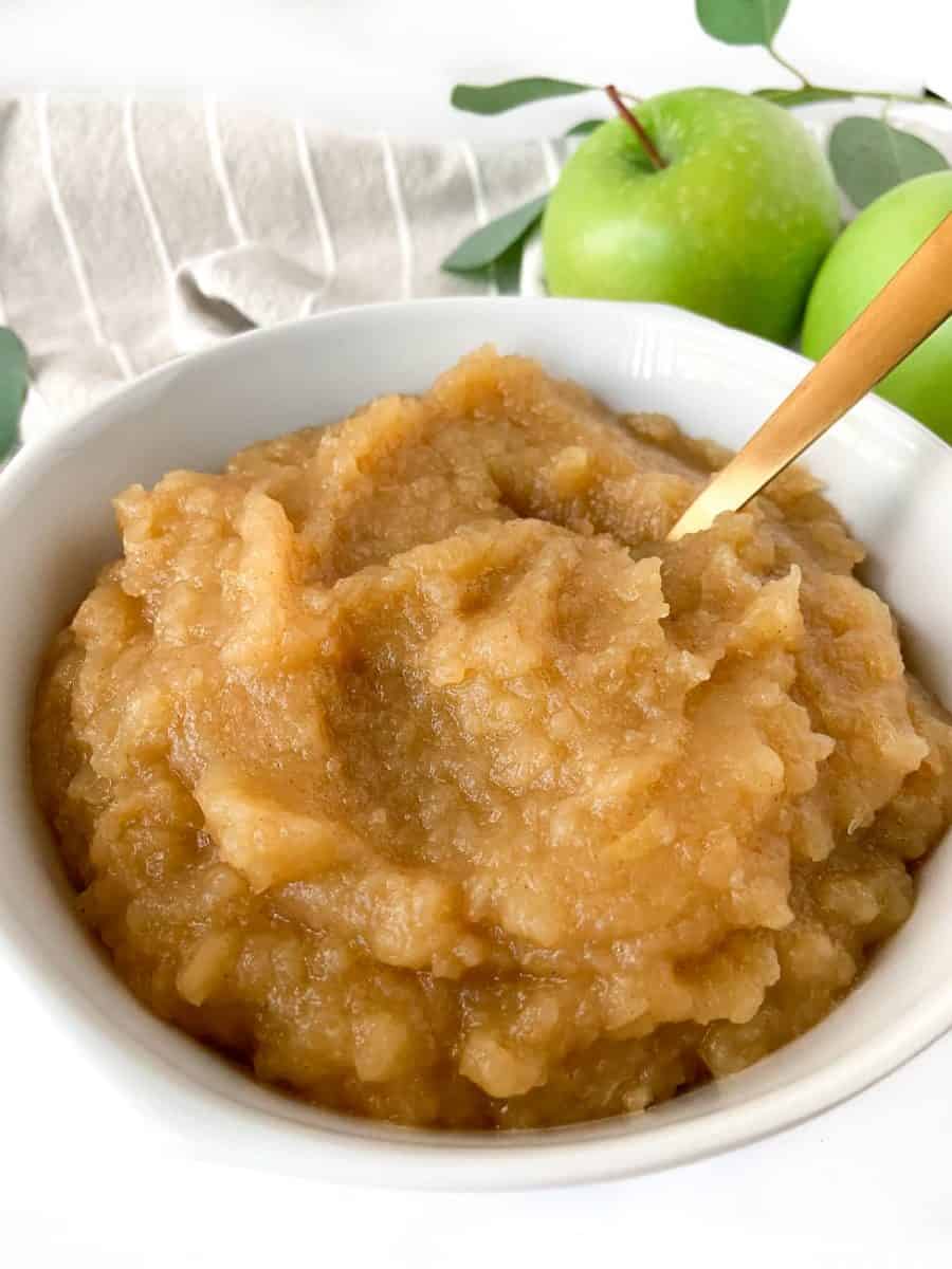 A white bowl with applesauce and a golden spoon. 