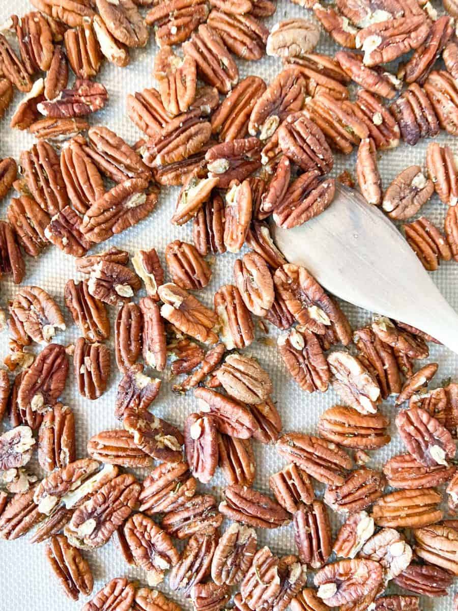 A silpat lined tray of completed pecans with a wooden spoon. 