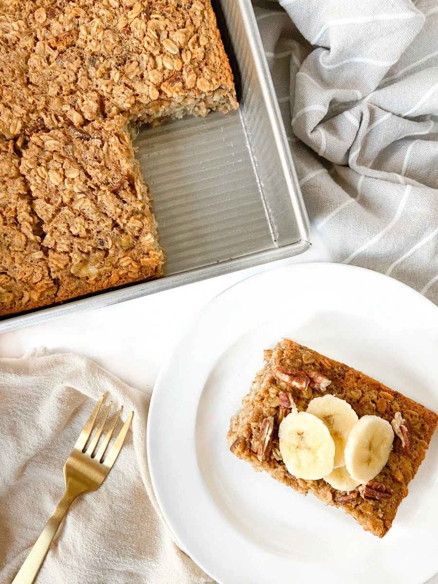 A tray of baked oatmeal and a single slice topped with banana slices on a white plate. 
