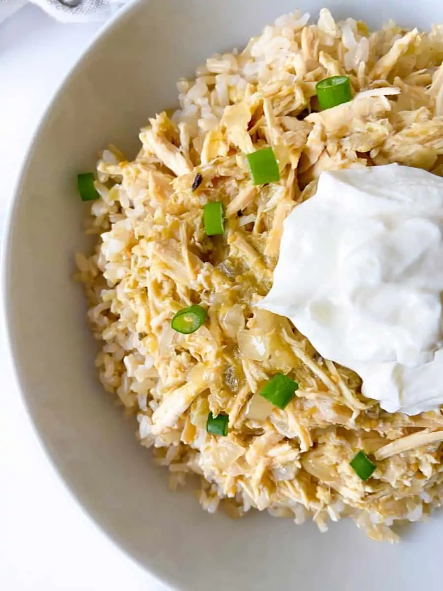 A bowl of rice topped with salsa verde chicken, greek yogurt, and scallions.