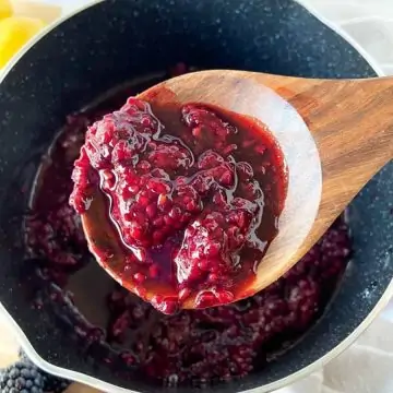 Photo of spoonful of Blackberry compote in wooden spoon being held over bowl