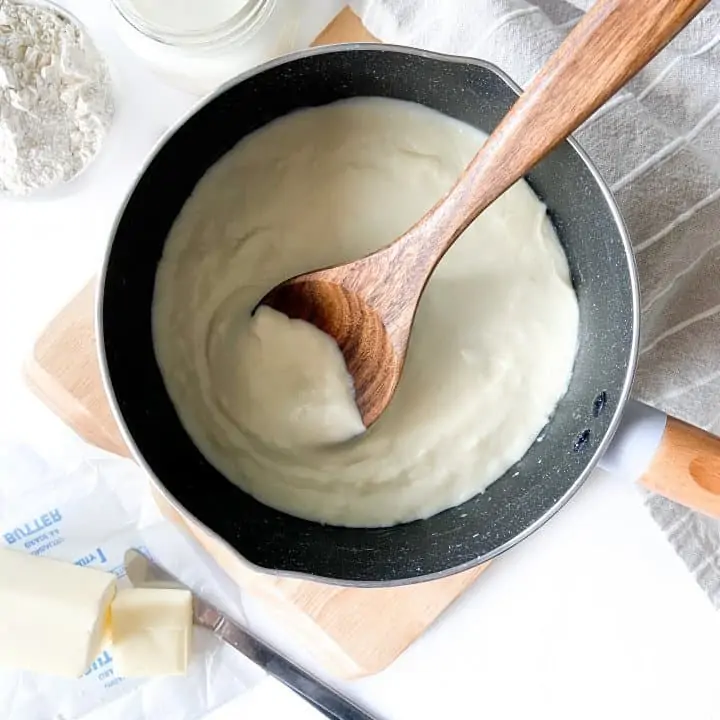 Bechamel sauce in bowl with wooden spoon.