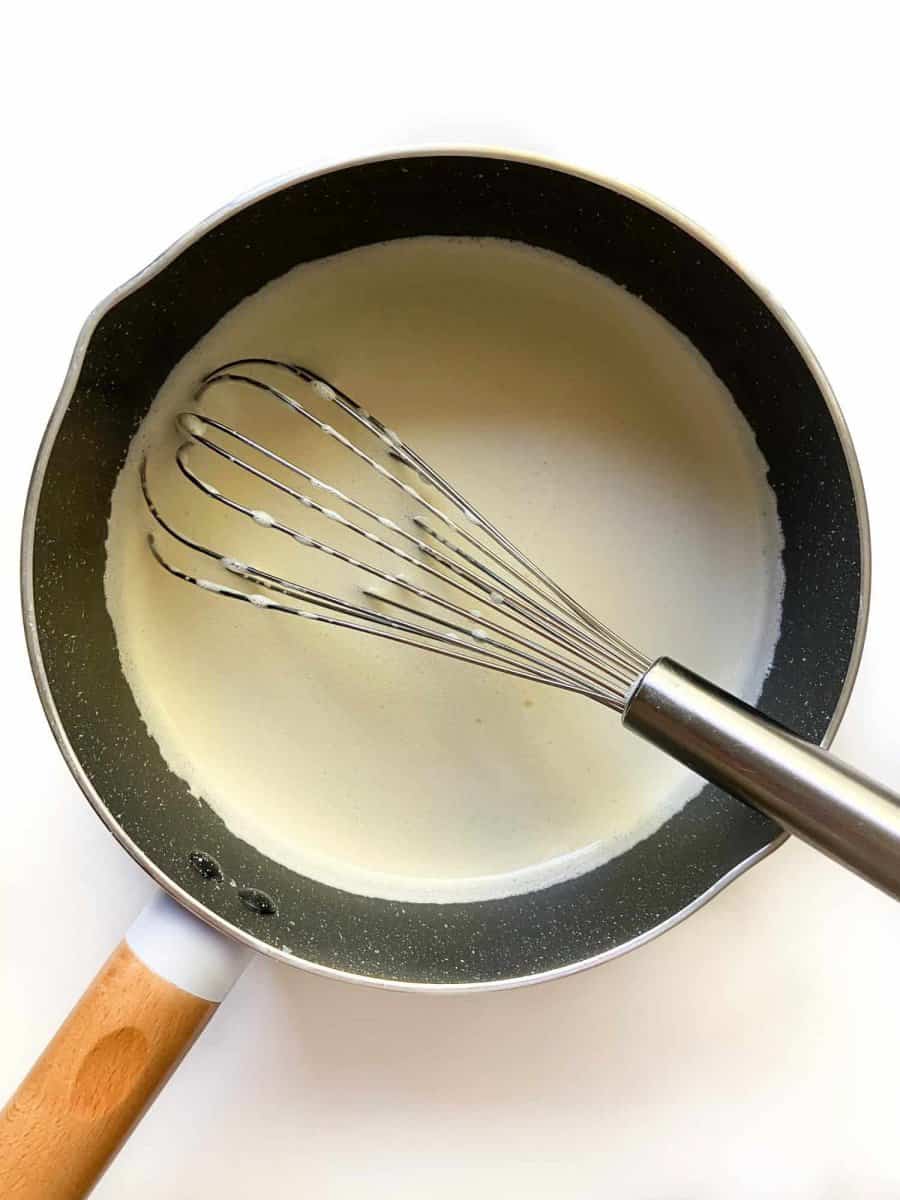Tempered egg yolk mixture in a small saucepan with a whisk.