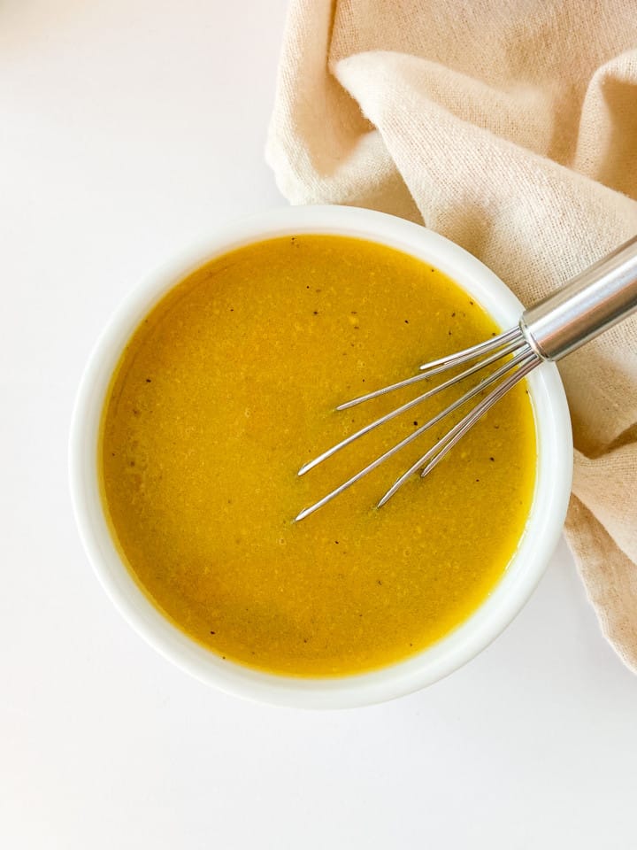 A small white bowl of salad dressing with a whisk. 