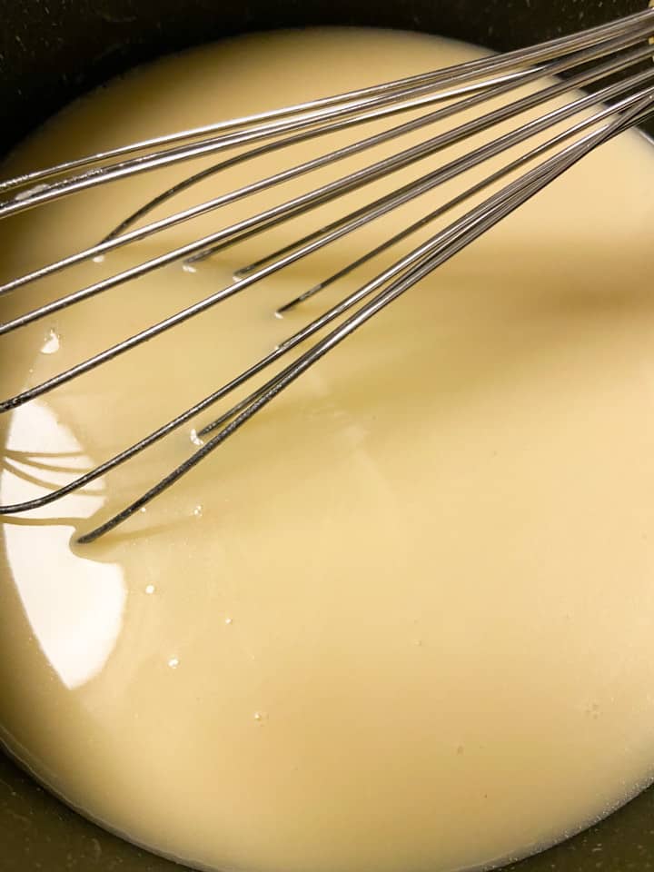 Chicken stock added to a roux in a small saucepan with a whisk. 