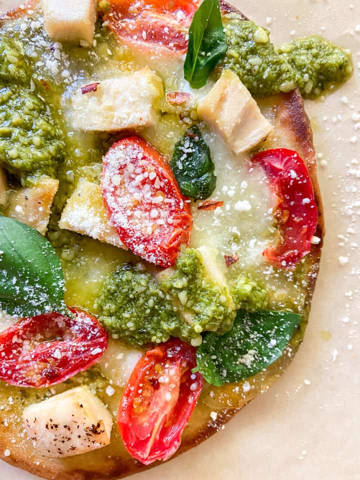 A close-up of a naan pizza garnished with grated parmesan and additional pesto. 