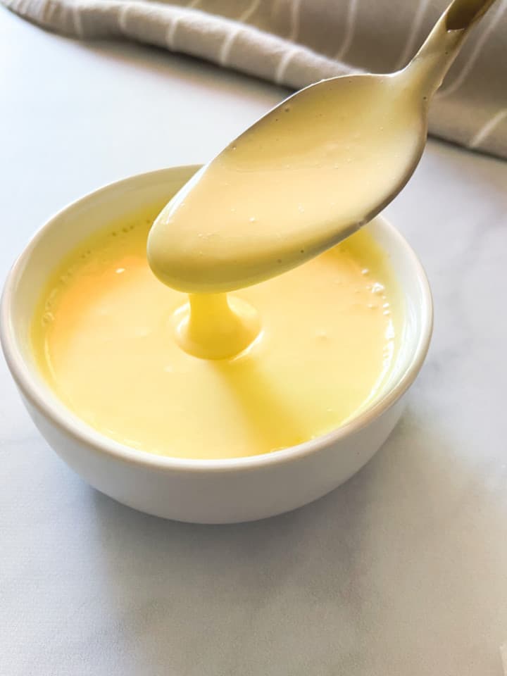 A small white bowl full of sauce with a spoon dipping into it. 