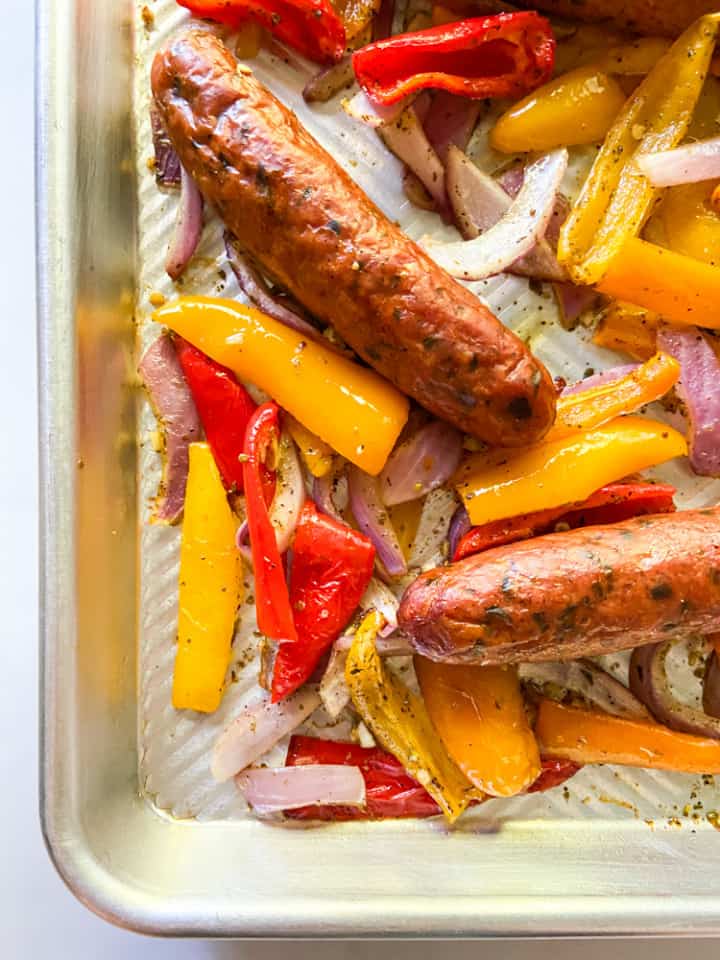 A close-up picture for cooked sausage, peppers, and onions on a sheet pan. 