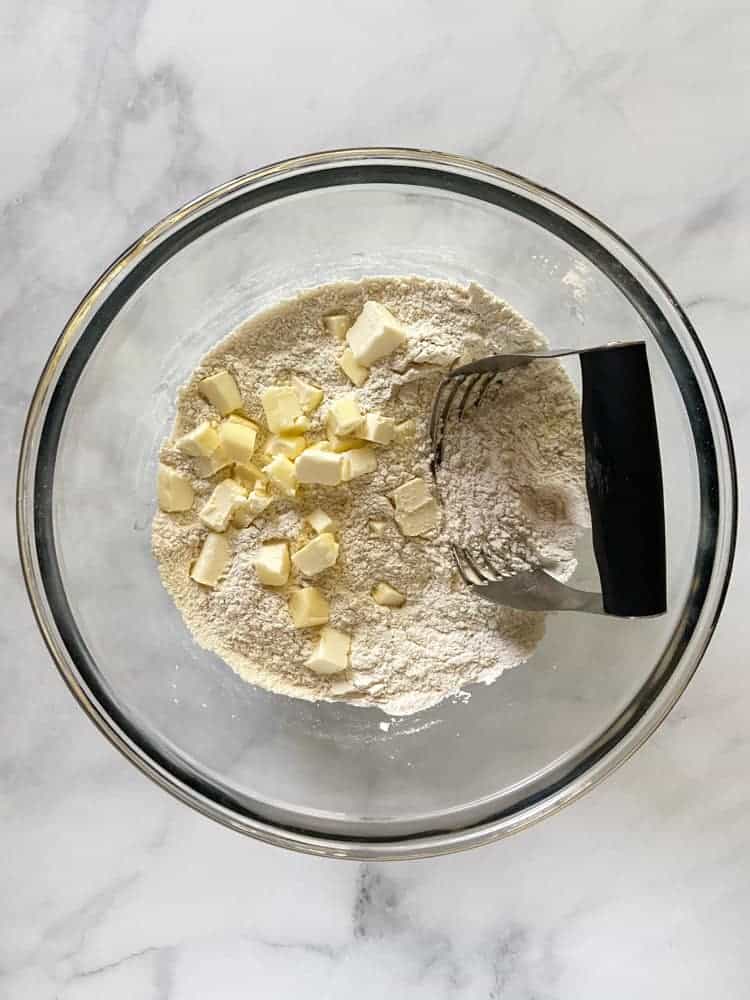 Flour in a bowl with cubes of cold butter and a pastry blender.