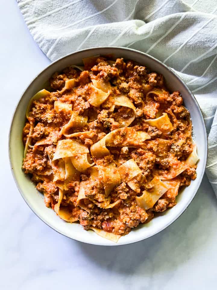 A large bowl of pappardelle pasta smothered in bolognese sauce and garnished with grated parmesan cheese. 