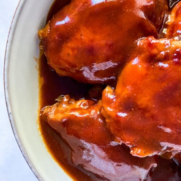 A close-up of a bowl full of BBQ chicken thighs smothered in BBQ sauce.