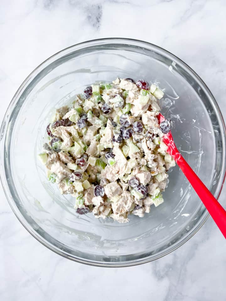 A clear bowl with a spatula and chicken salad.