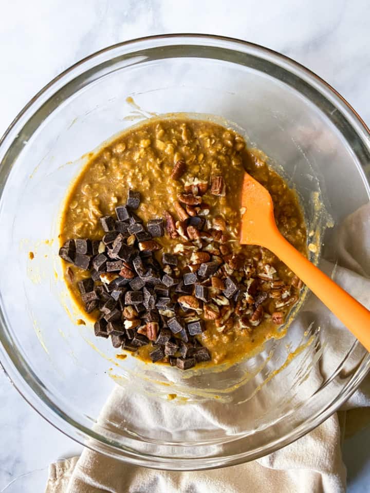 A clear bowl filled with the pumpkin-oat mixture along with chocolate chunks and pecans.