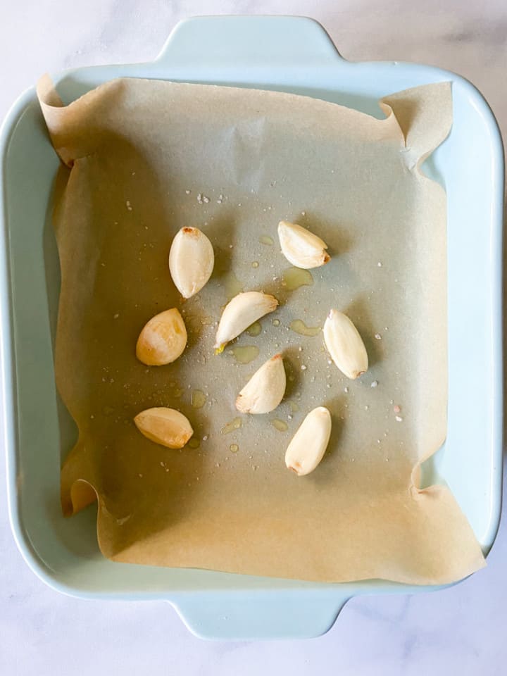 A parchment lined dish with olive oil covered garlic cloves.
