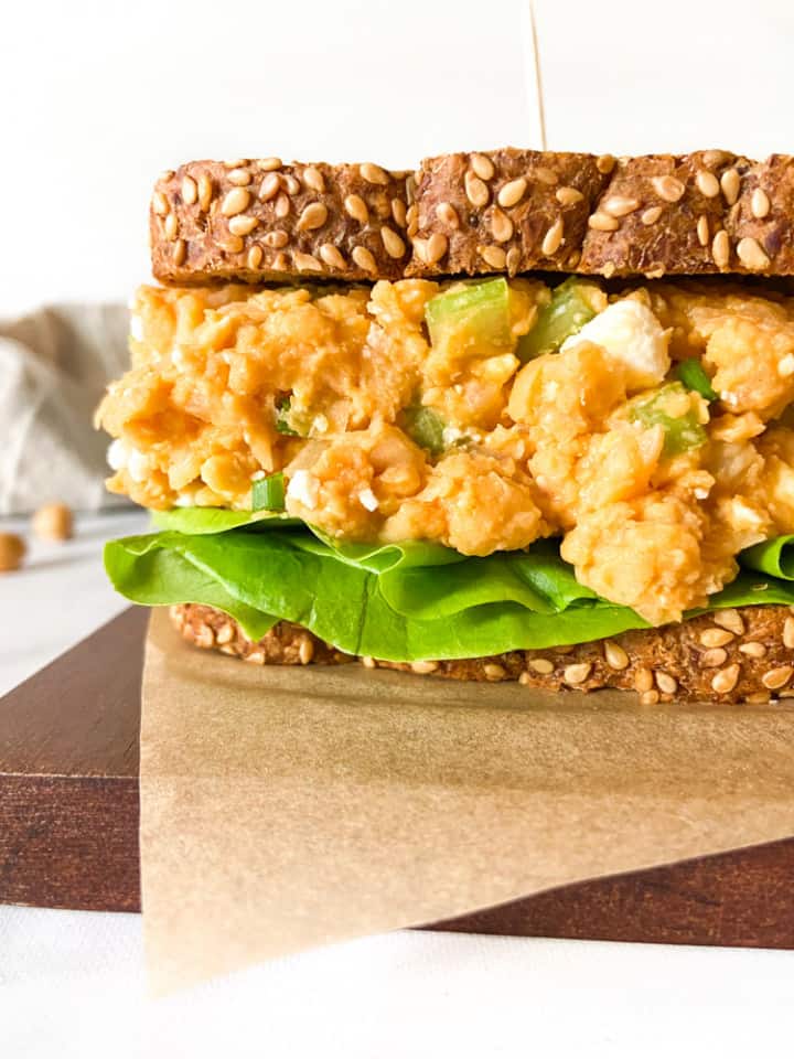 A smashed chickpea salad sandwich with sesame bread on a parchment-lined board.