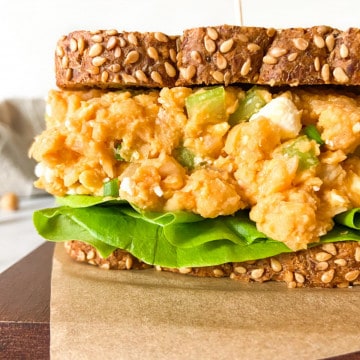 A smashed chickpea salad sandwich on a parchment-lined board.