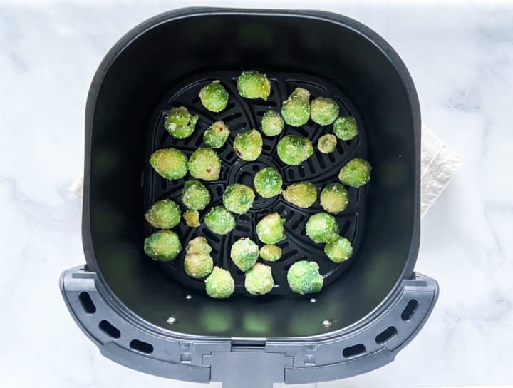 Uncooked brussel sprouts and garlic in an air fryer basket.