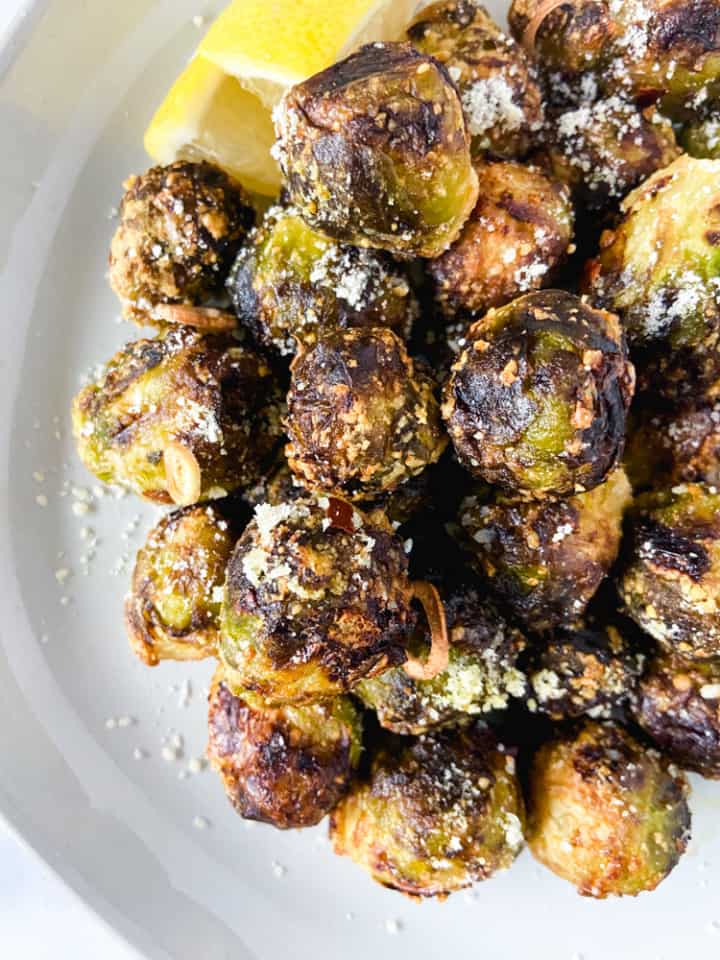 A close-up image of crispy brussel sprouts on a plate with lemon wedges.