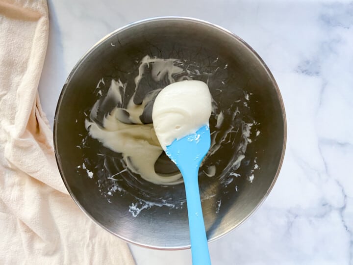 A bowl of completed cream cheese icing with a blue spatula.