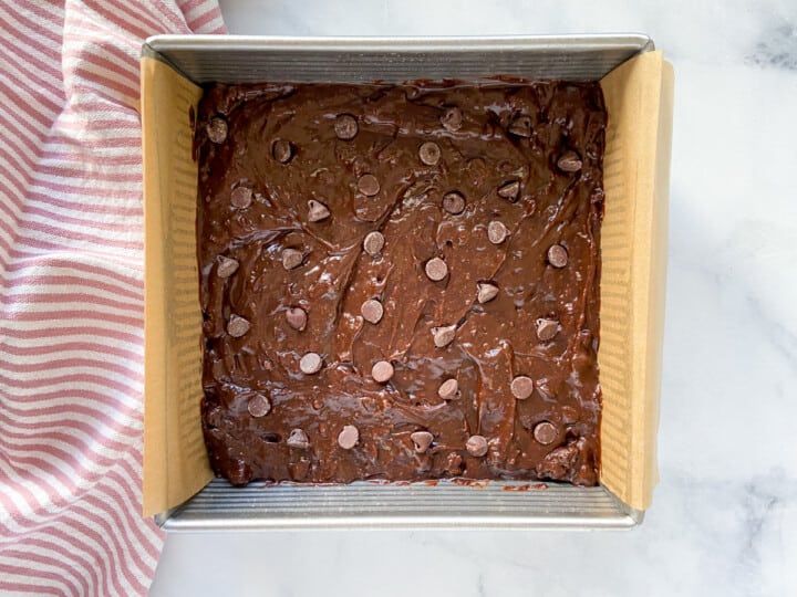 Brownie batter spread into a baking pan dotted with chocolate chips.