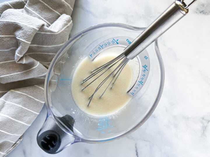 The liquid ingredients mixed together in a liquid measuring cup with a whisk.