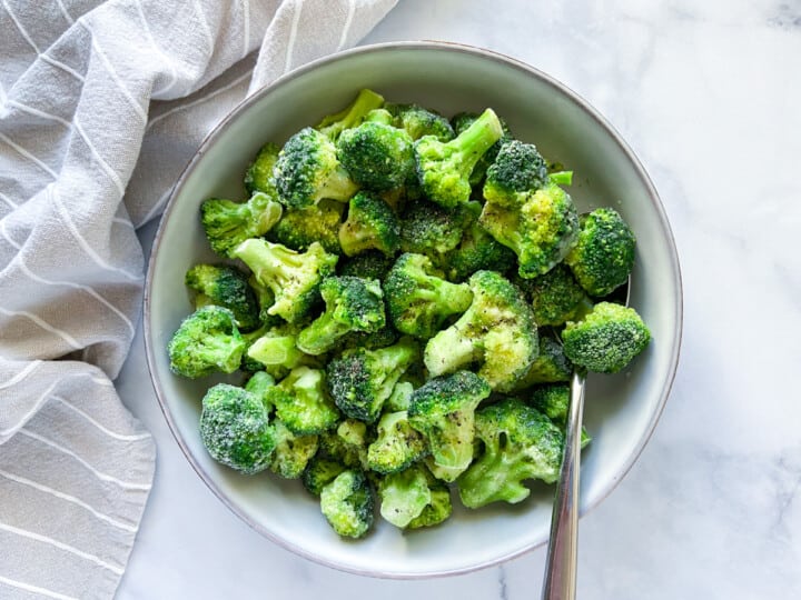 Frozen broccoli florets in a bowl with a spoon.