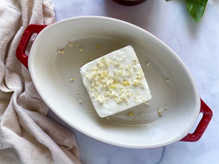 A block of feta covered in garlic in a baking dish.