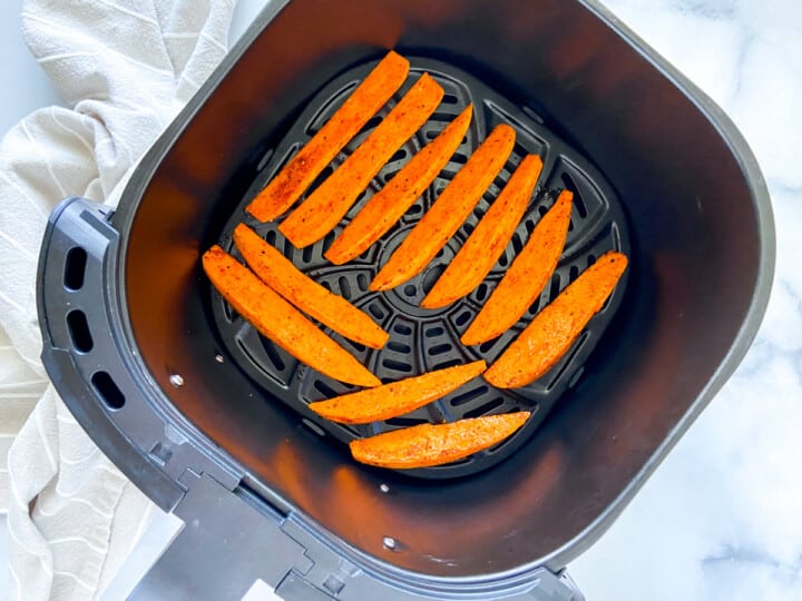 Seasoned sweet potato wedges in an air fryer basket.