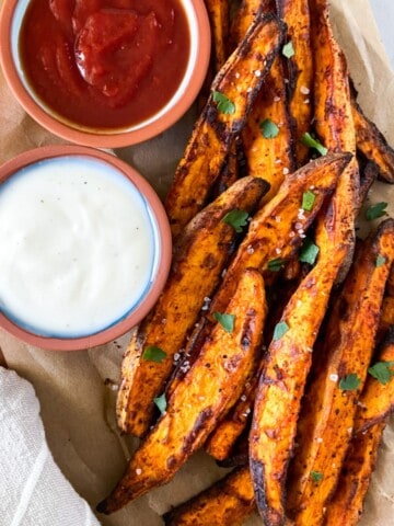 Cooked sweet potato wedges on a parchment lined tray with sauces.