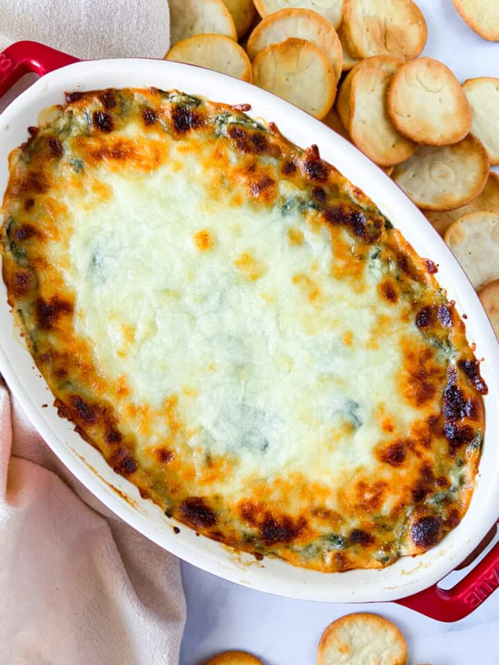 Hot spinach dip in an oval dish surrounded by pita chips.