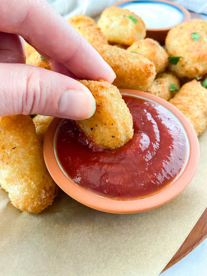 A hand dipping a tot into ketchup.
