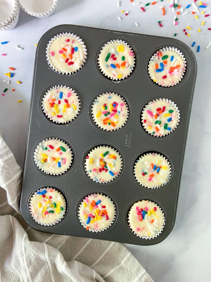 A tray of bite-sized cheesecakes with rainbow sprinkles.