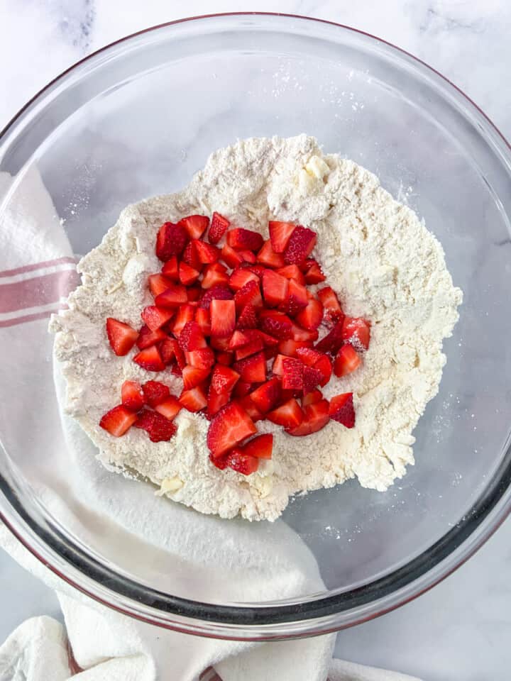 Dry ingredients in a bowl with butter cut in and strawberries.