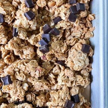 Peanut butter granola clusters with chocolate chunks on a parchment-lined tray.