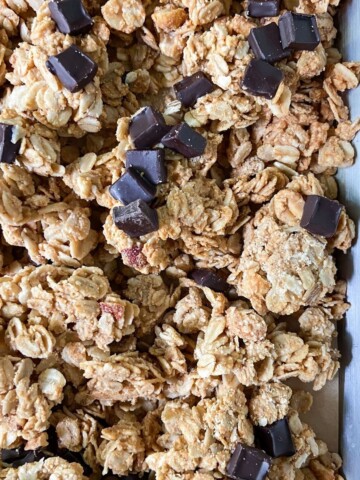 Peanut butter granola clusters with chocolate chunks on a parchment-lined tray.