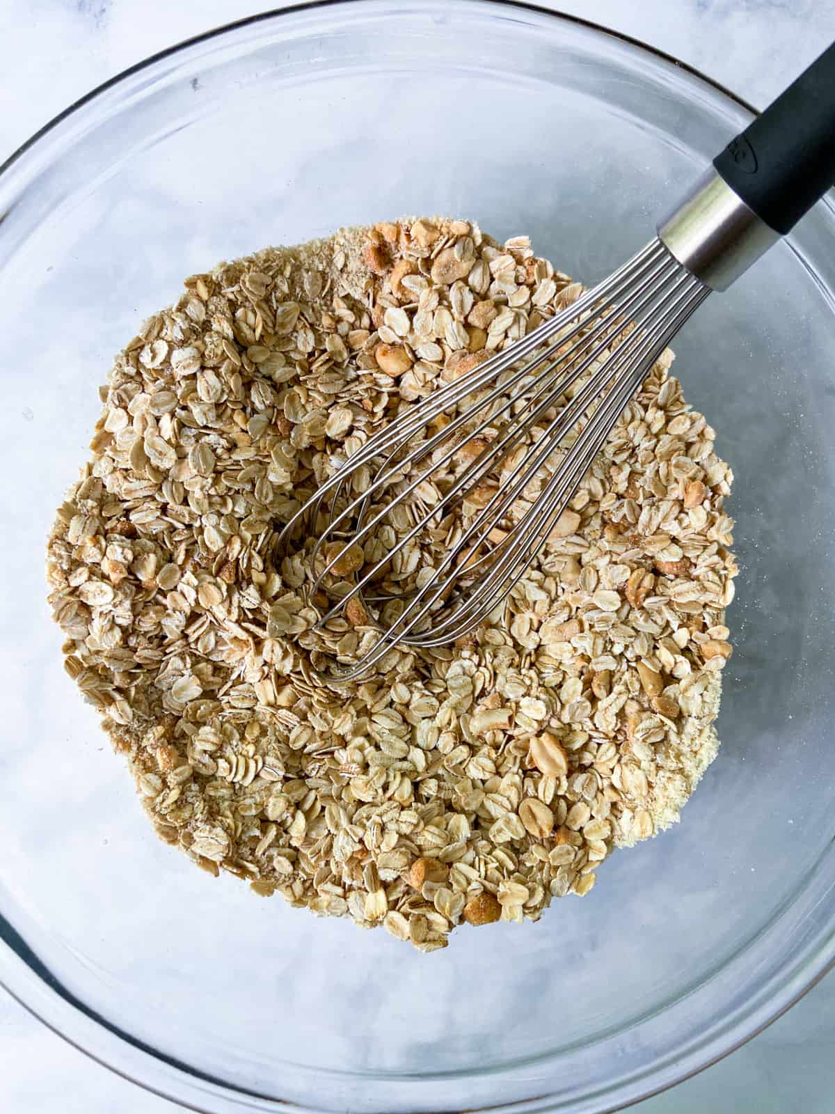 Oats, almond flour, and peanuts with a whisk in a bowl.