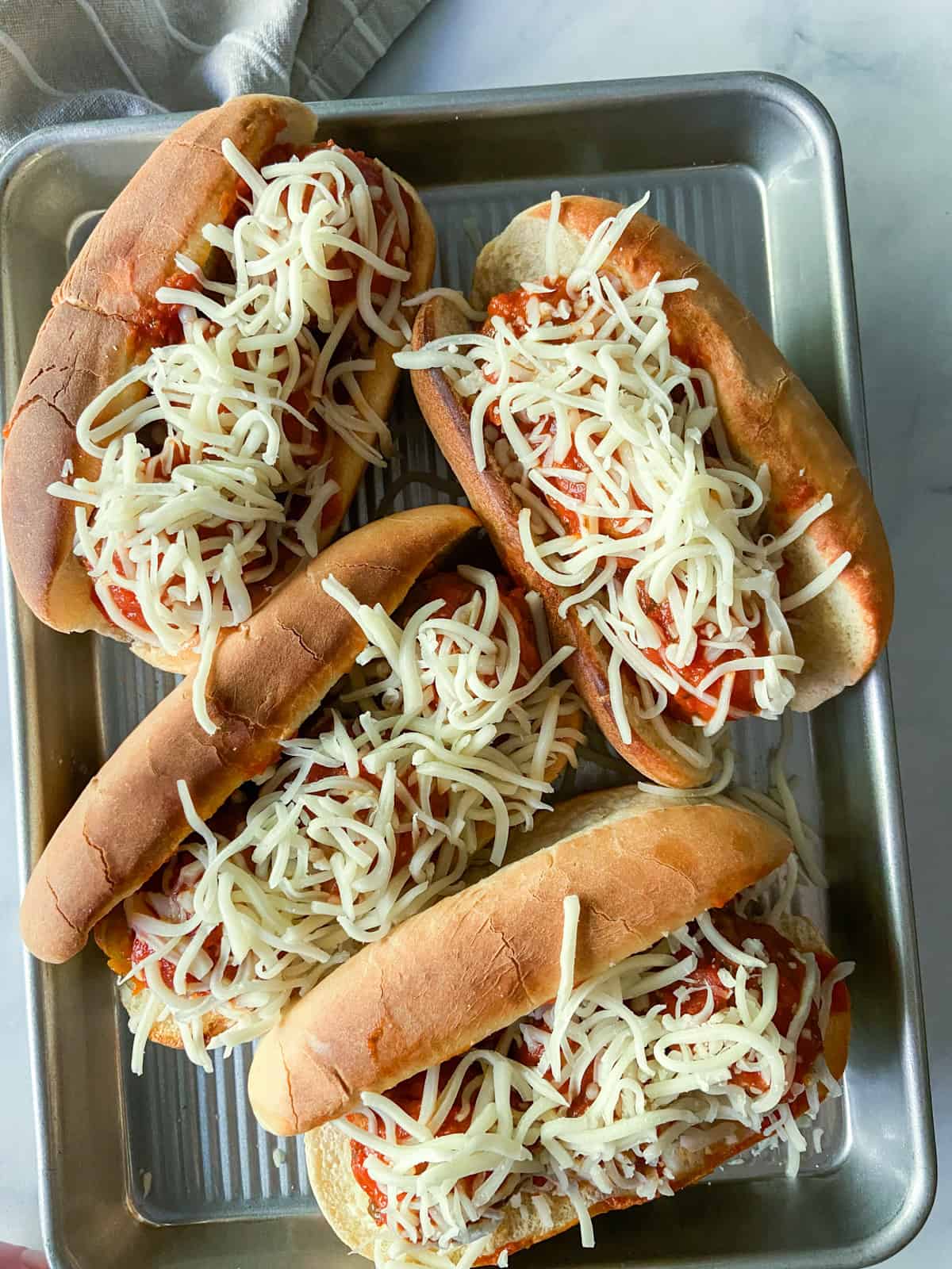 Un-broiled meatball subs covered in shredded cheese on a sheet tray.