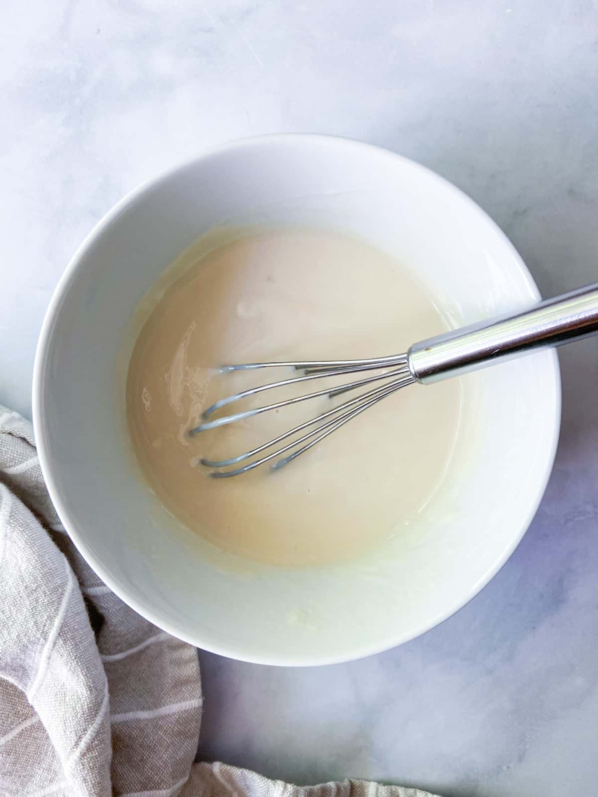 Sweetened condensed milk mixture in a bowl with a whisk.