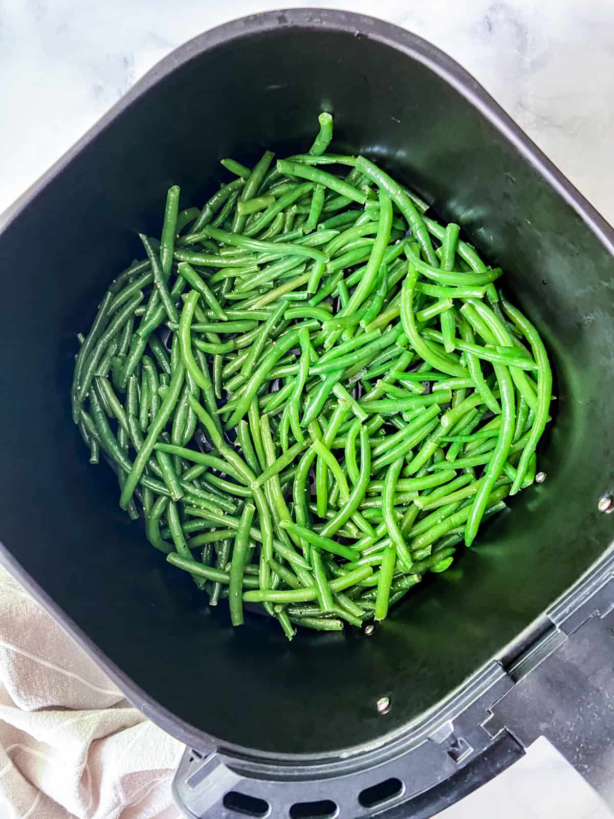 Uncooked green beans in an air fryer basket.
