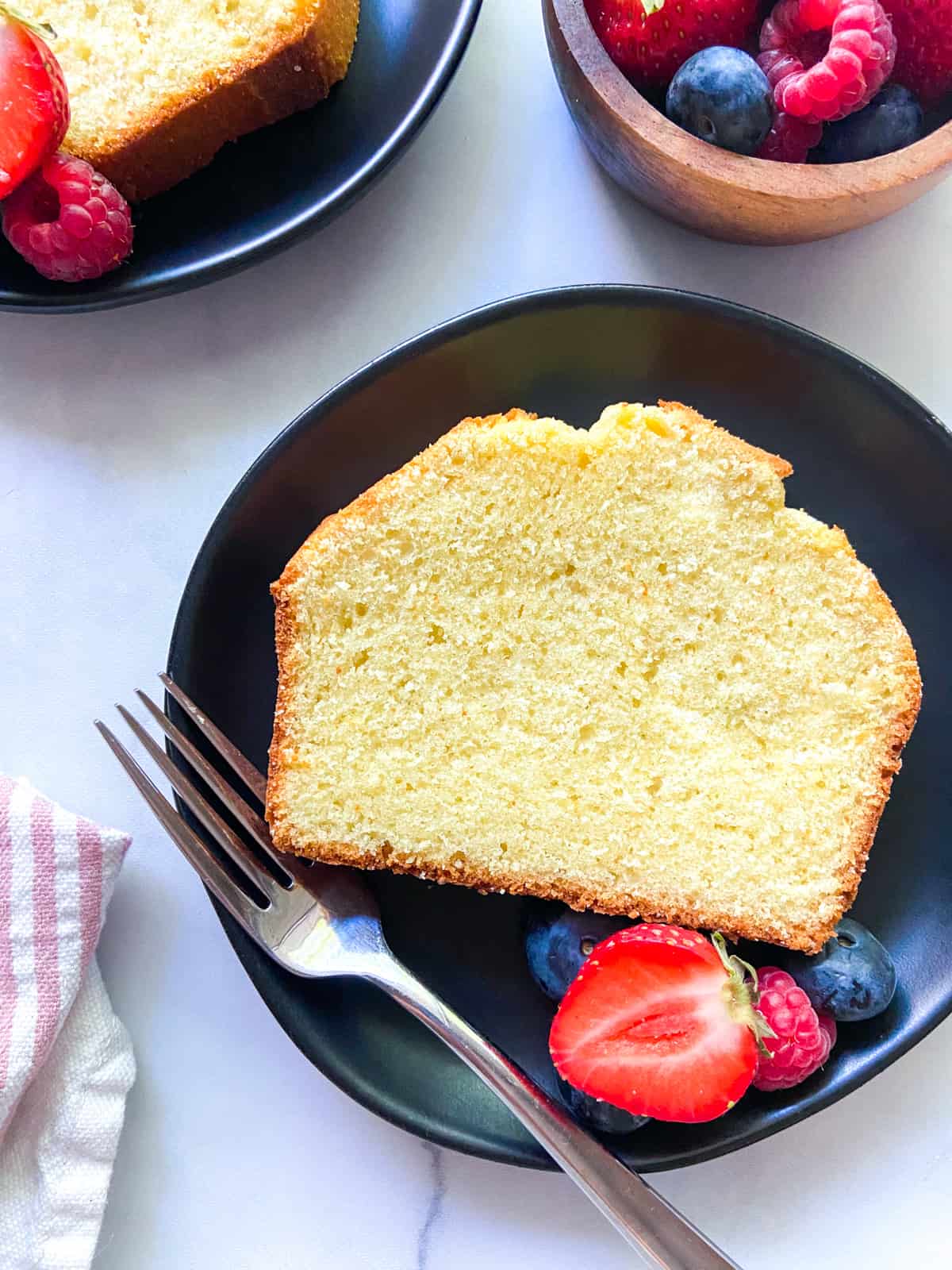 A slice of vanilla buttermilk pound cake on a plate with berries.