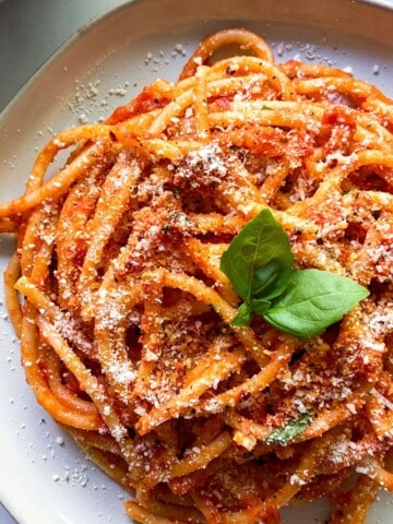 A plate of bucatini pomodoro garnished with basil.