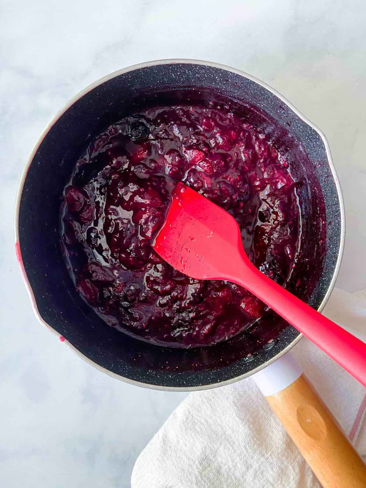 Berry compote in a saucepan with a spatula.